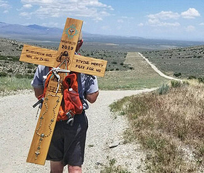 On his back he carries one of two handmade wooden crosses he made for the journey.